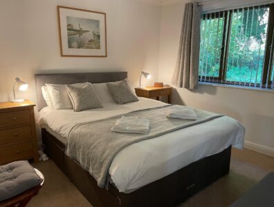 There is a double bed with two matching sets of drawers and reading lights on both sides of the bed. The curtains are open revealing a nice green view. The bed has 2 pristine white towels on the bed.
