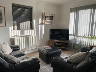 The sun is coming through the window into the stylish lounge that has a flat screen TV, and black leather sofas