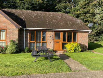 The Front of Cottage 25 showing a wooden picnic bench on the front lawn on a sunny day